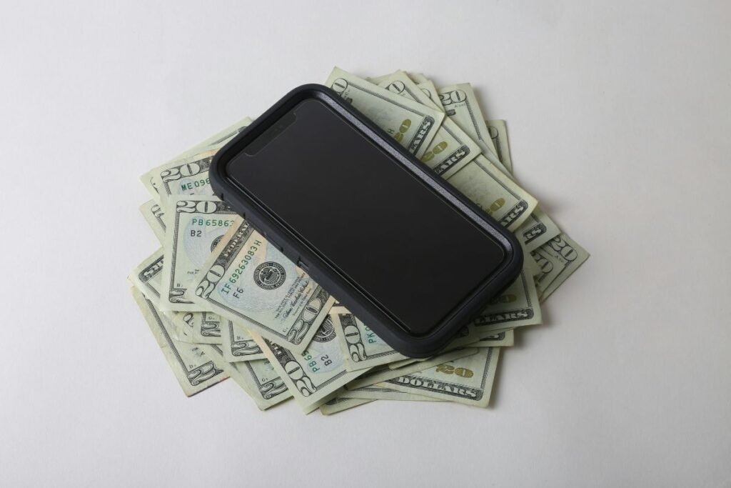 Smartphone placed on scattered twenty dollar bills representing mobile job earnings and work from home income