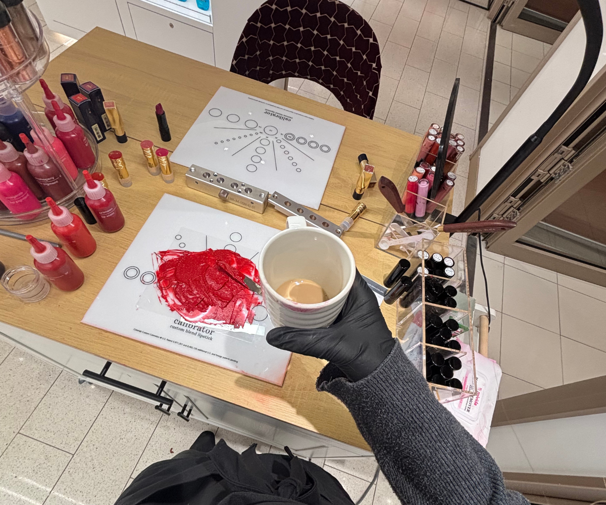 Overhead view of custom makeup blending station on cruise ship showing colorant chart, red lipstick pigment being mixed, makeup supplies, and professional setup for blend-your-own makeup side hustle