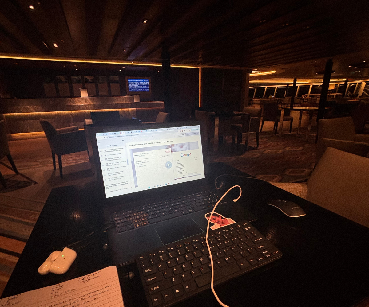 Laptop open on a table in a dimly lit restaurant or lounge, displaying a blog setup page, with handwritten notes and a pen beside it for planning blog content