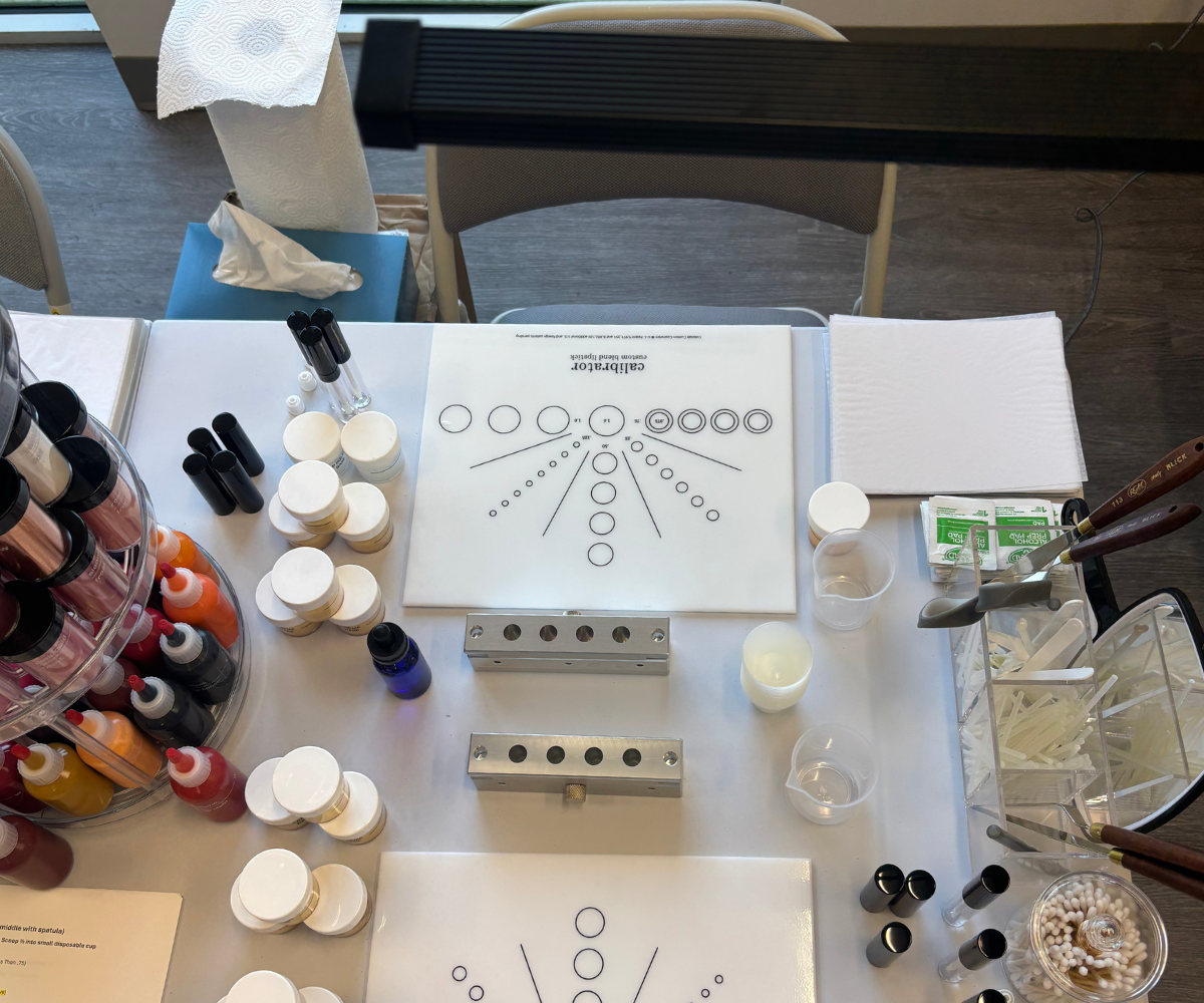 Makeup and lipstick blending workspace with white circular containers arranged around printed worksheets showing a calibrator to measure pigments